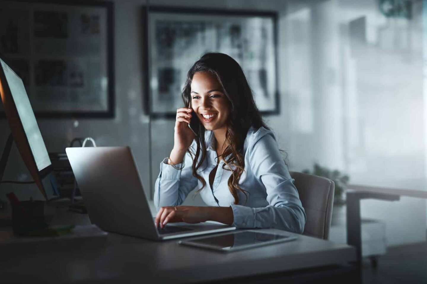 Kvinna pratar i telefon framför dator