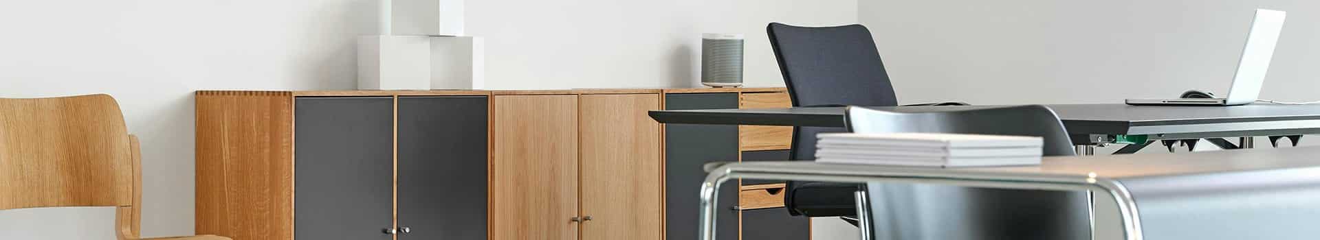 Modernt kontor med trästolar, skåp, skrivbord, laptop och staplade papper. Ljust och minimalistiskt.